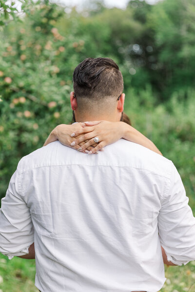 engaged couple posing with woman's hands around man's neck showcasing pearl engagement ring