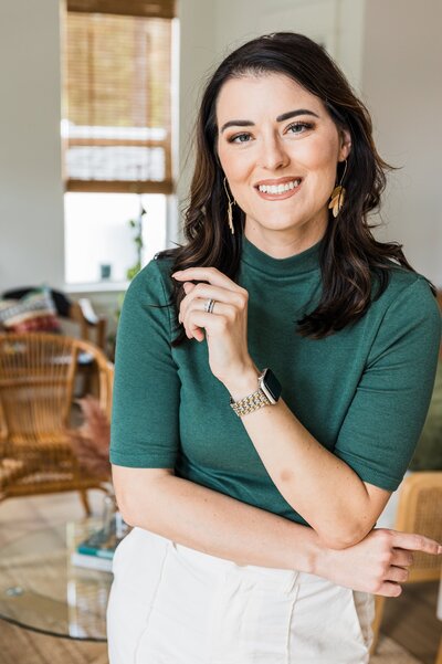 Kaley Marie, brand photographer, sits on a desk with arms crossed during a lifestyle headshot at her brand session in a studio in Orlando.