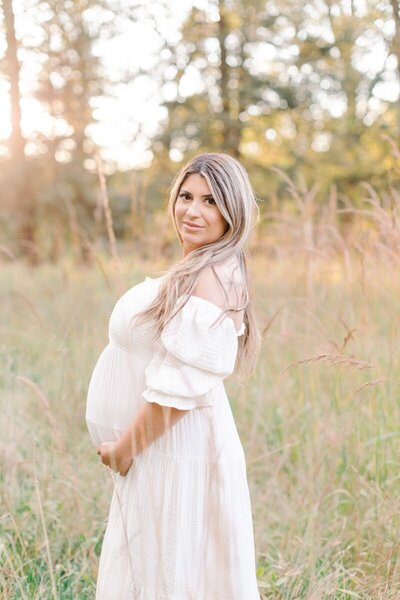 A pregnant woman stands in a field holding her pregnant belly during her maternity photos in New Jersey