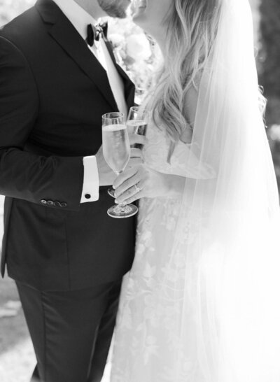 Gentleman in wedding suit and her wife in wedding gown celebrate their unification with a glass of champagne.