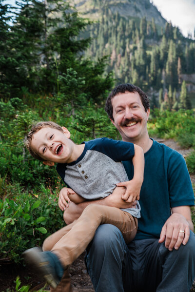 Candid photo of boy and his Dad at Tipsoo Lake in Mount Rainier National Park for adventure family photography session blue color scheme family photo outfits
