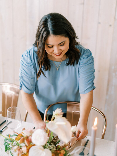 Woman in a blue top smiling and arranging a table setting