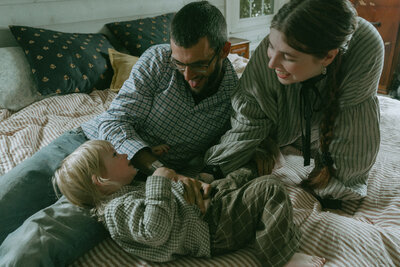 couple lying on bed with son during family photography session by Elsie Goodman 