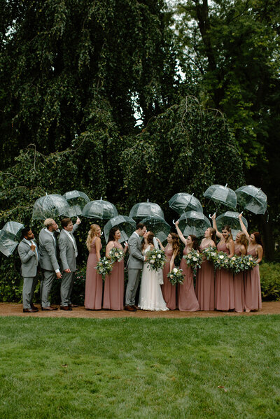 wedding party celebrates the bride and groom as they kiss under umbrellas