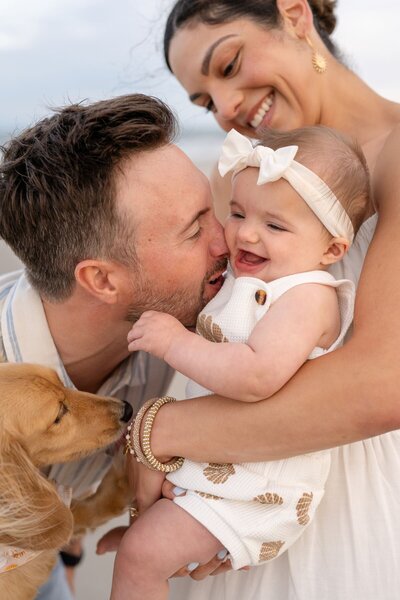 mother holding toddler while father kisses her and holds their family dog