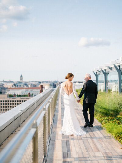 low back wedding gown with long sleeves, bride and groom walking on the rooftop of the international spy museum in washington dc photographed by dc wedding photographer omar & comany