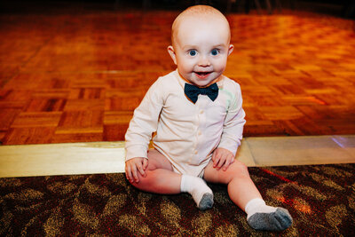 Baby with blue eyes sitting on dance floor at wedding reception