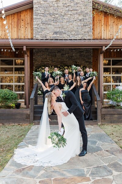 Groom dips his bride for a kiss as their wedding party cheers