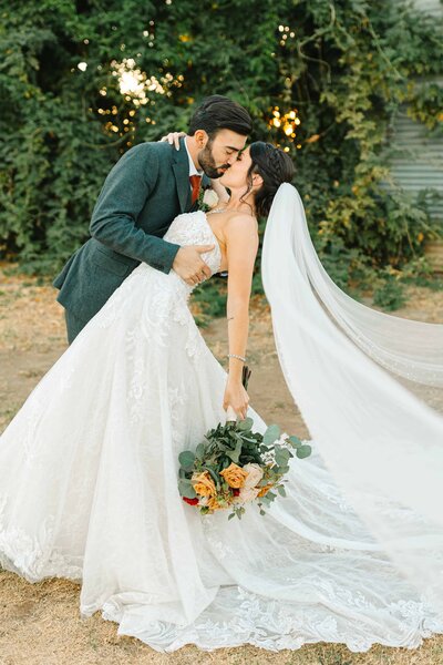 Bride and groom kissing during sunset at Wolf Lakes wedding venue in Sanger while the brides veil blows into the camera