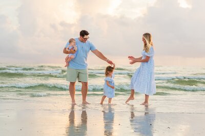 adorable family photo  on the beach, playing in the waves at sunset with baby and toddler