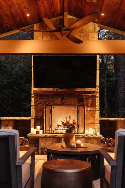 Covered patio with a custom stone outdoor fireplace, mounted TV, and cozy ambient lighting, designed by Better Lawns and Gardens for outdoor living in Arkansas.