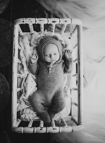 A tiny little newborn baby girl smiles as she's carefully posed and swaddled in a photography prop.