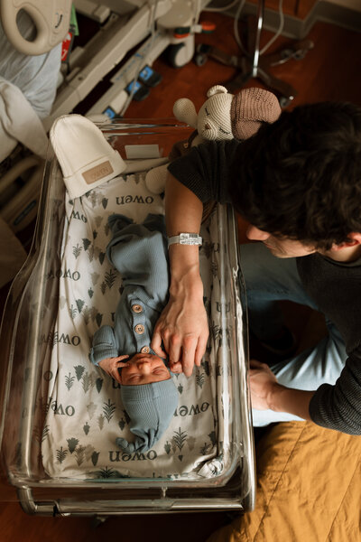 Fdad holding newborn baby's hand in hospital