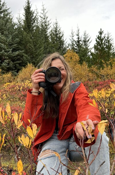Adventure photographer Stephanie Vermillion in red coat and jeans outside holding camera
