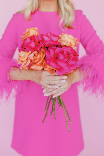 Woman in bright pink dress with feather sleeve cuffs holding a pink and orange bouquet