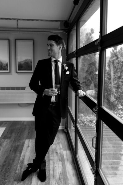 black and white photo of groom leaning against a window
