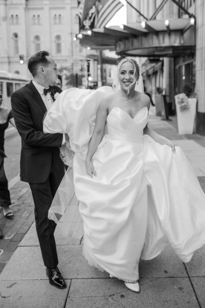 Newlywed couple crossing the street in center city in Philadelphia. The groom is carrying the bride's dress train.