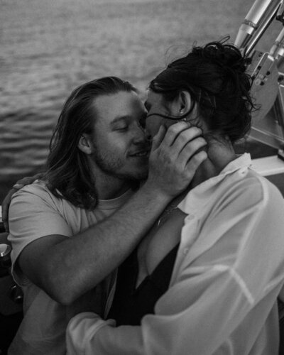 black and white image of a couple kissing on a boat with the sea in the background.