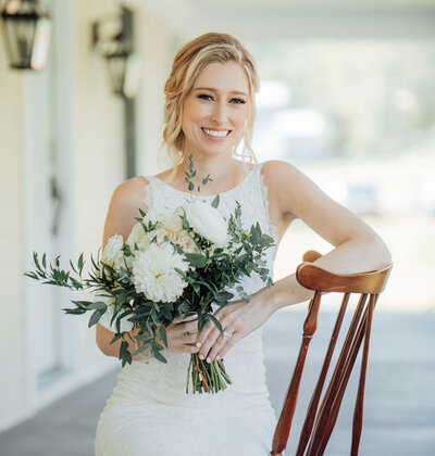 Bride posing on porch with flowers and vintage chair | Summer Wedding at Wagar Farm | Ellenville, New York