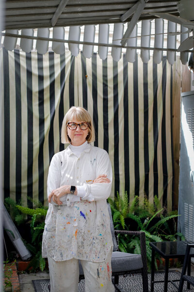Adele walking on patio wearing paint covered artist smock