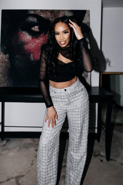 Tiara in a black top and sparkly pants posing and touching her hair