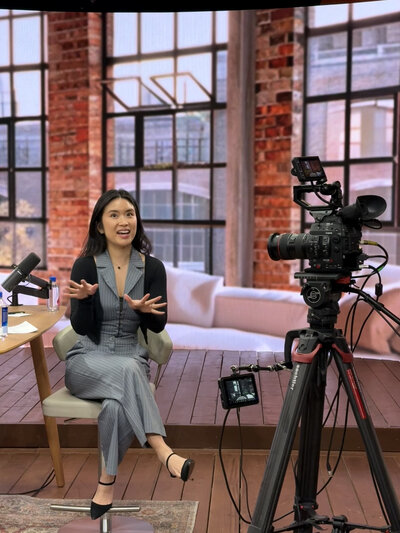Stephy Chen guest speaking in a bright industrial-style studio, seated in front of a camera setup during a video shoot.