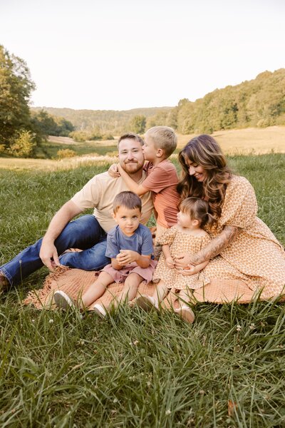 Family of five sitting on a blanket in  a field.