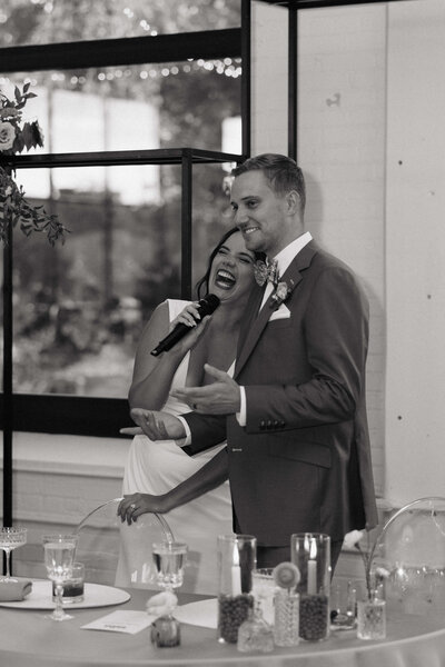Laughing bride leans into groom during their wedding speech.