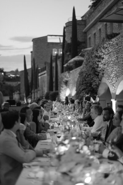 Black and white photo of a Bastide de Gordes wedding dinner featuring a long, rectangular table, soft candlelight and medieval architecture