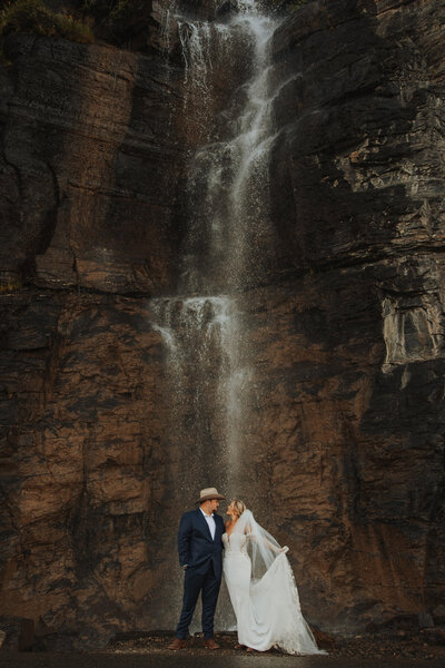 Bride and groom smiling at each other in front of a waterfall during their Montana wedding day.