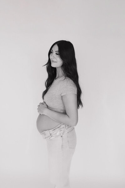 The pregnant girl is standing sideways and has her hand on her belly.