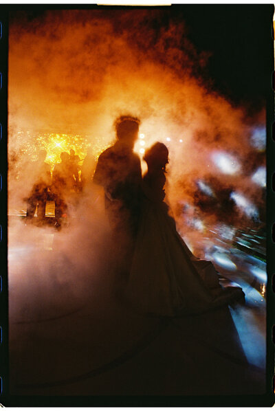 a bride and groom having their first dance in orange backlit fog on film