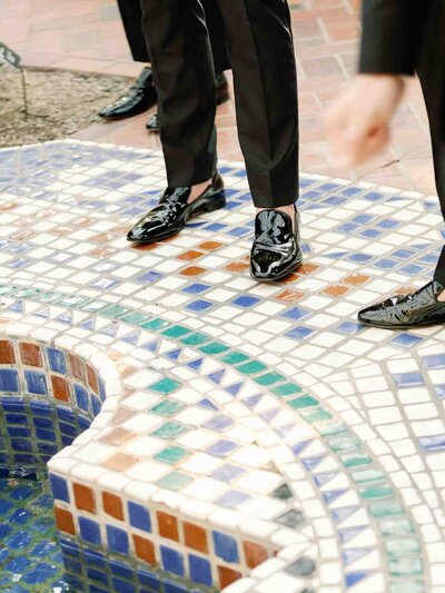 Close-up of groom's polished black shoes on colorful mosaic tiles.