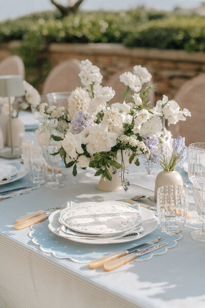 Blue and white ticking stripe wedding table with blue scalloped place mats, pearl cutlery, hand-painted round wedding menus, speckled glassware, mini sage green table lamps and lush white centerpieces between blue hyacinth accent flowers