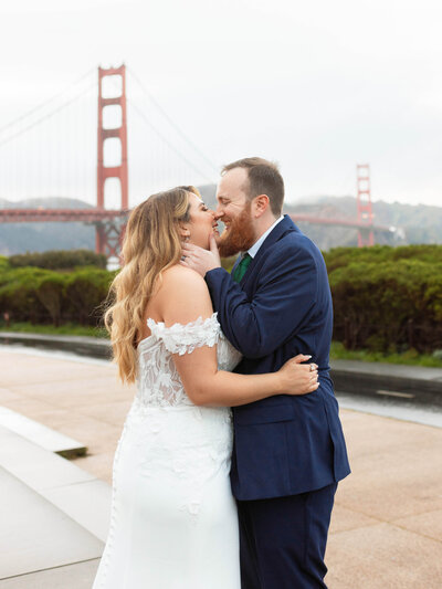 Newlyweds laugh after they kiss in front of the Golden Gate Bridge in San Francisco, CA.