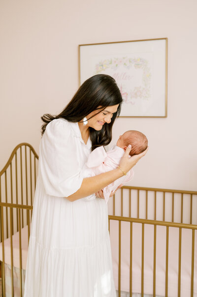 Couple poses with newborn baby girl in pink and white nursery during in-home newborn session