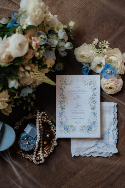 flatlay out wedding invitation, bridal bouquet and jewelry