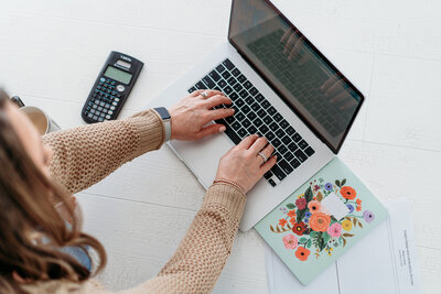 Kim typing on her laptop with a calculator next to her