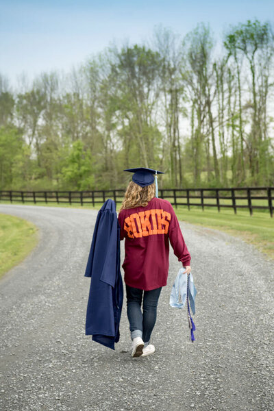 senior girl walking away with cap and gown in hand