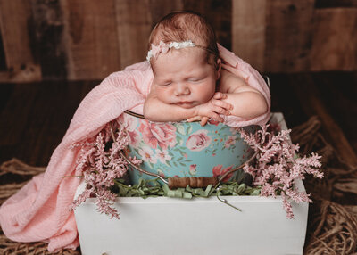 A baby with a flower crown on place in a floral basket.