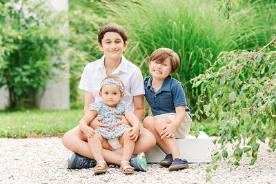 Two brothers and a sister sitting on a white box for family photos.