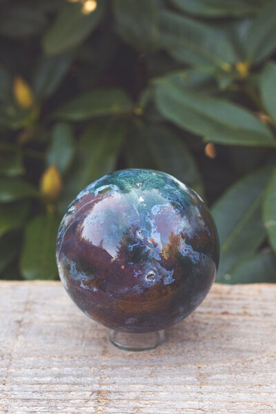 The front side of a moss agate sphere crystal with deep teal, blue, and green colours.