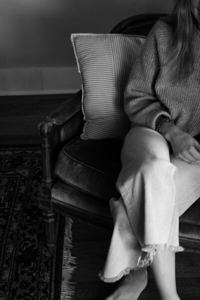 Black and white photo of a woman sitting on a couch with her head resting on a pillow, representing emotional exhaustion, overwhelm, and the support offered through group coaching for women.