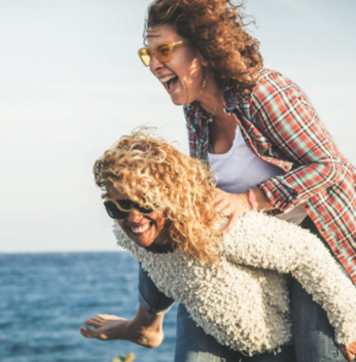 People playing piggy back on a beach in midlife showing how they are still young at heart at 50+