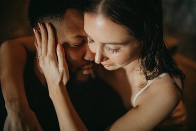 Close-up of an intimate couple’s embrace, with eyes closed and foreheads touching in a moody, emotional setting.