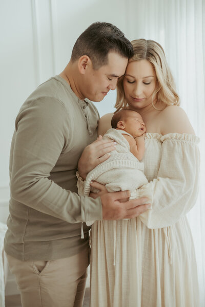 Mum and dad forehead to forehead and nose to nose while mum is holding sleeping baby on her chest.