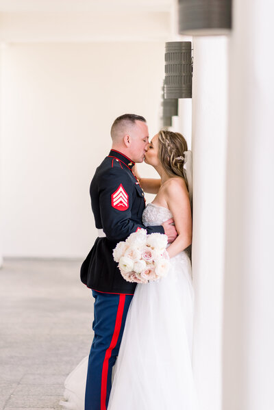 Groom and bride kissing against a pillar