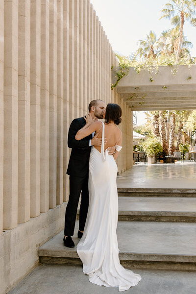 Bride and groom share a kiss on the stone steps at Acre Resort, framed by palms and modern design.