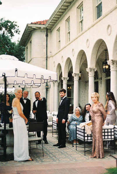 Film photo of wedding guests standing underneath umbrellas and sitting outside