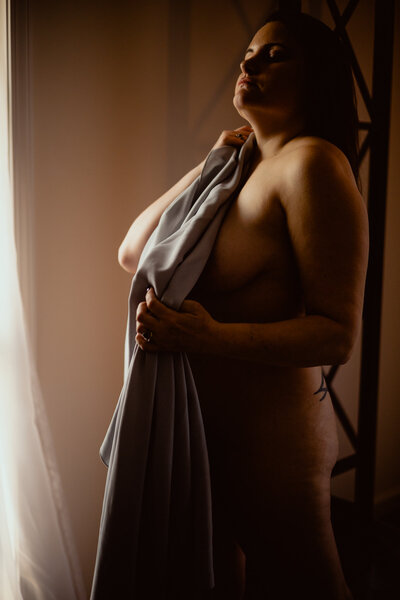 Knoxville boudoir photo of woman holding a sheet by a window
